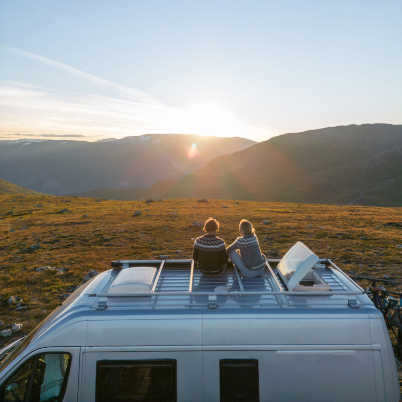 Drone shot Road trip concept- Couple on the roof of a motorhome watching sunset, autumn